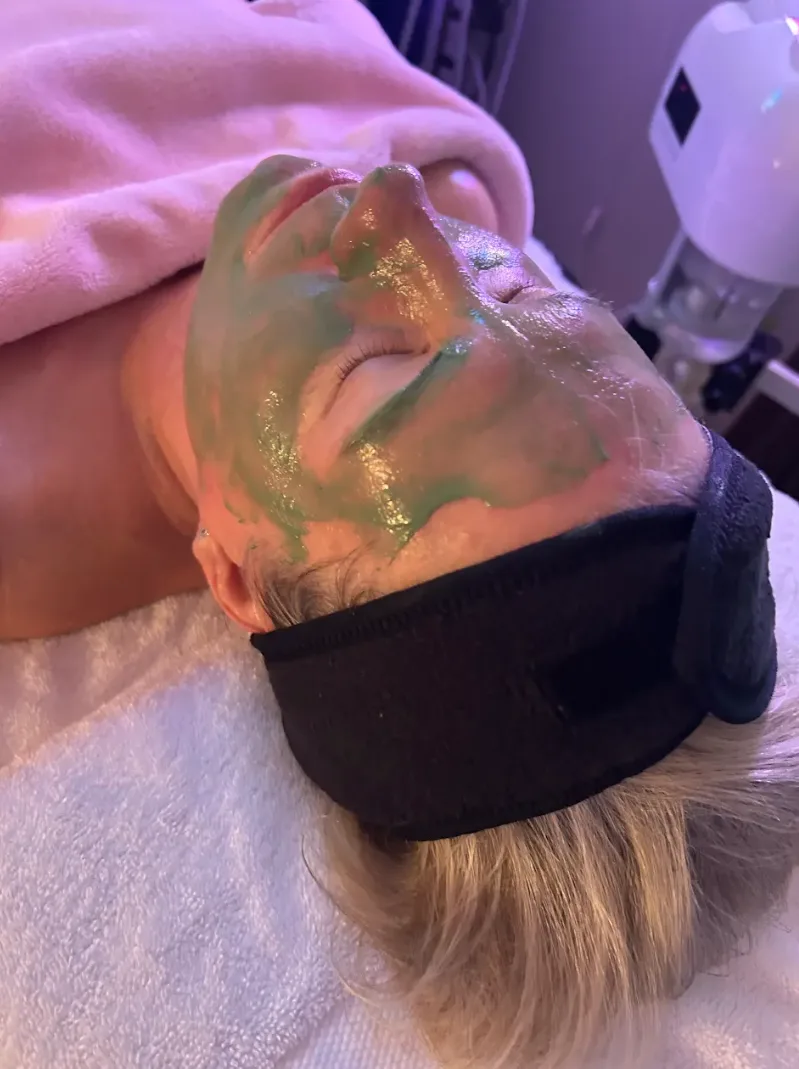 Client relaxing under a green treatment mask during a glow facial