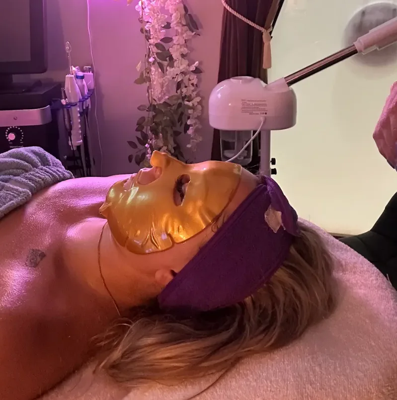 Client under a gold sheet mask with the steamer beside her