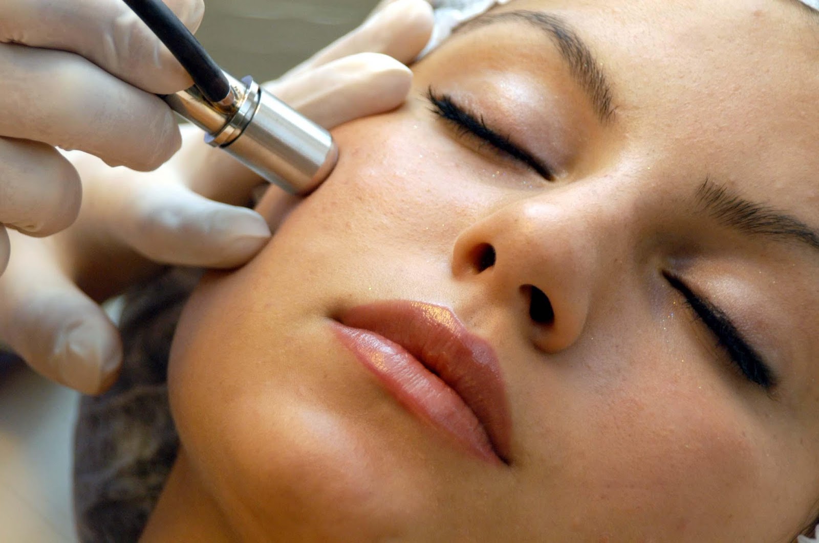 Esthetician passing a microdermabrasion wand along a client's cheekbone